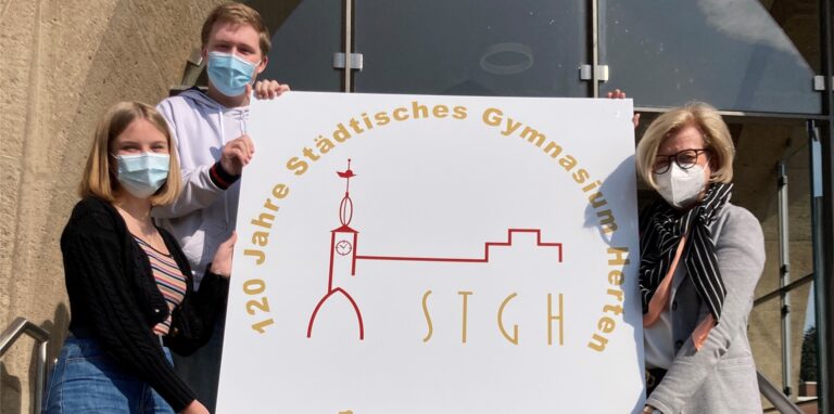 Zum 120-jährigen Bestehen des Städtischen Gymnasiums Herten am 1. Mai 2021 haben Schülersprecherin Anika Troska und stellvertretender Schülersprecher Maximilian Messmann, beide aus der Stufe Q1, gemeinsam mit Schulleiterin Bärbel Schweers ein Schild im Innenhof aufgehängt. Hier zeigen sie es im Vorfeld vor dem historischen Eingangsportal.
