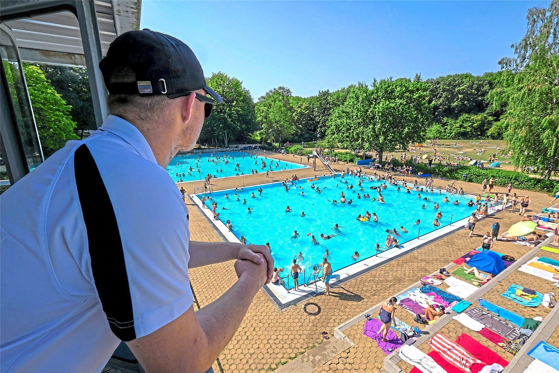 Ein Bademeister steht auf dem Wachturm im Südbad Recklinghausen. Im Becken und am Beckenrand tummeln sich hunderte Freibad-Gäste