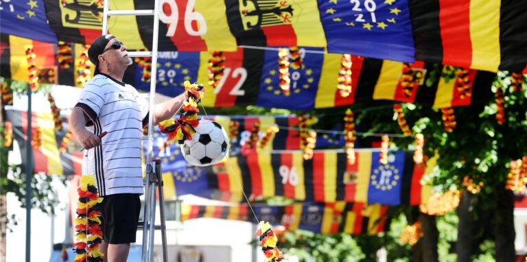 Der fußballverrückte Achim Klimmeck repariert in seiner zur Fußball Europameisterschaft mit über 500 Fahnen geschmückten Wohnstraße eine Seilverbindung.