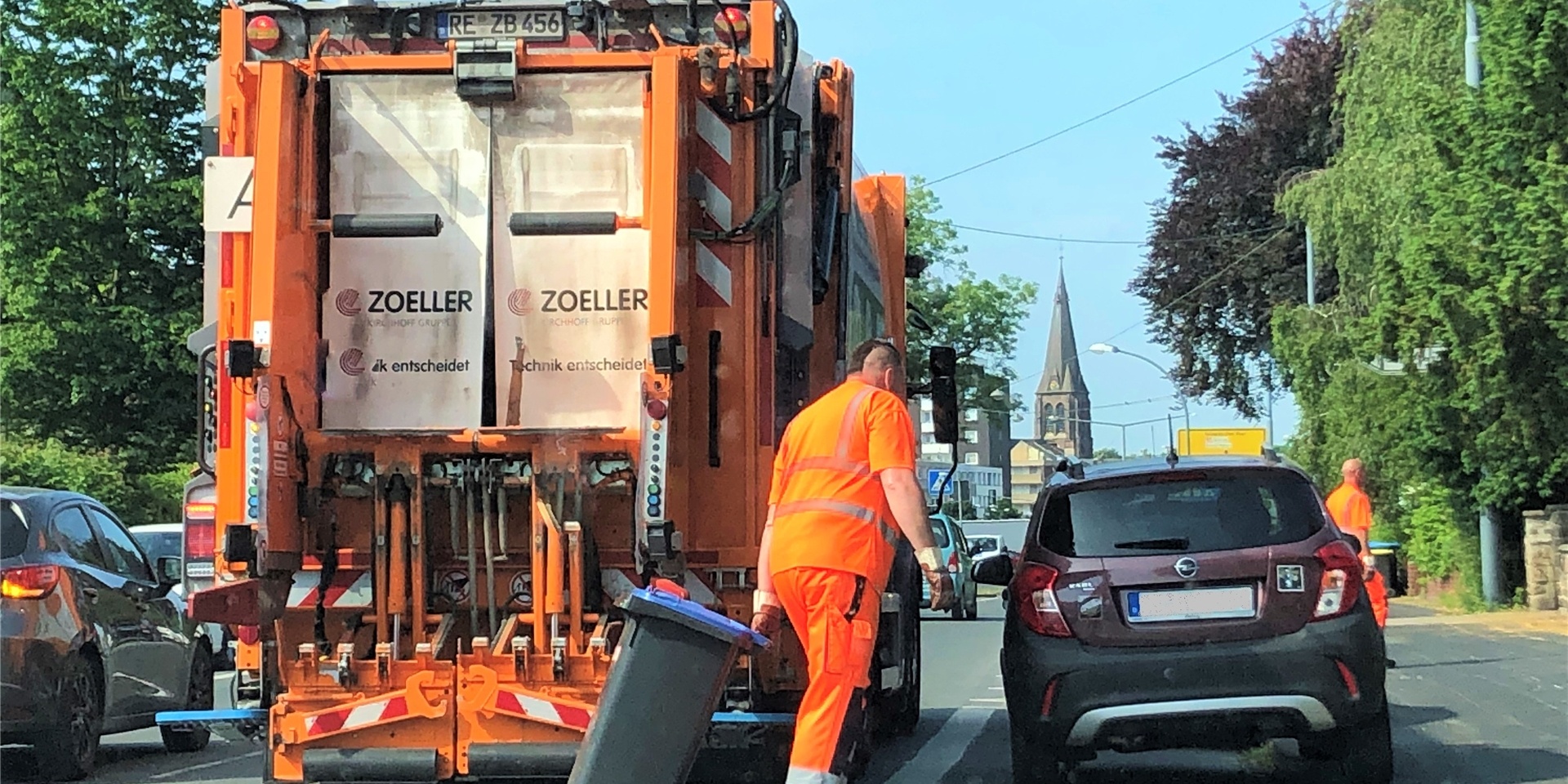 Ein Müllwerker zieht eine blaue Tonne hinter sich her, hinter ihm steht ein Müllfahrzeug.