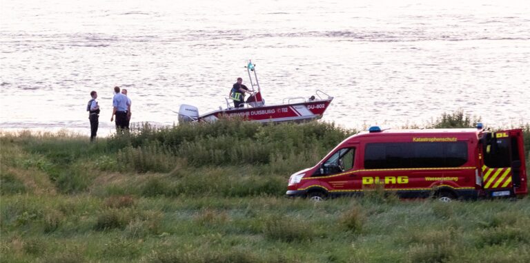 Einsatzkräfte der Polizei, Feuerwehr und DRLG arbeiten am Ufer des Rheins. Nach einem möglichen Badeunfall ist ein Mädchen gerettet worden. Zwei weitere werden noch vermisst.