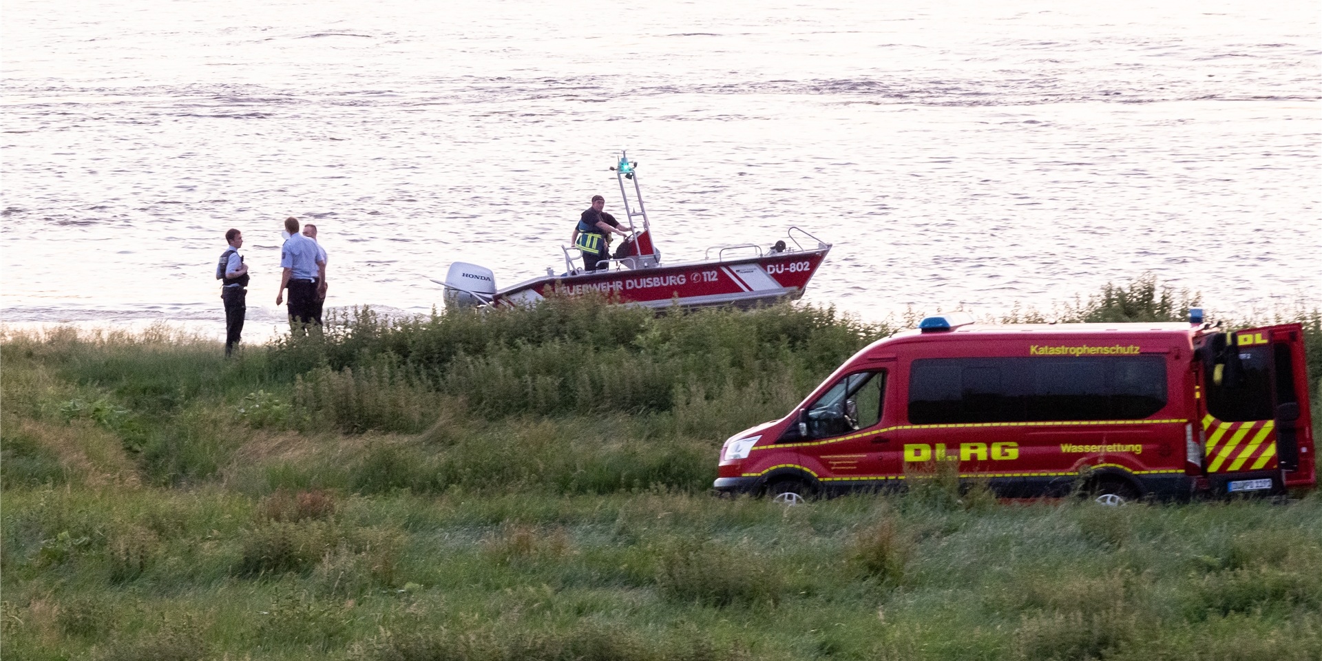 Einsatzkräfte der Polizei, Feuerwehr und DRLG arbeiten am Ufer des Rheins. Nach einem möglichen Badeunfall ist ein Mädchen gerettet worden. Zwei weitere werden noch vermisst.
