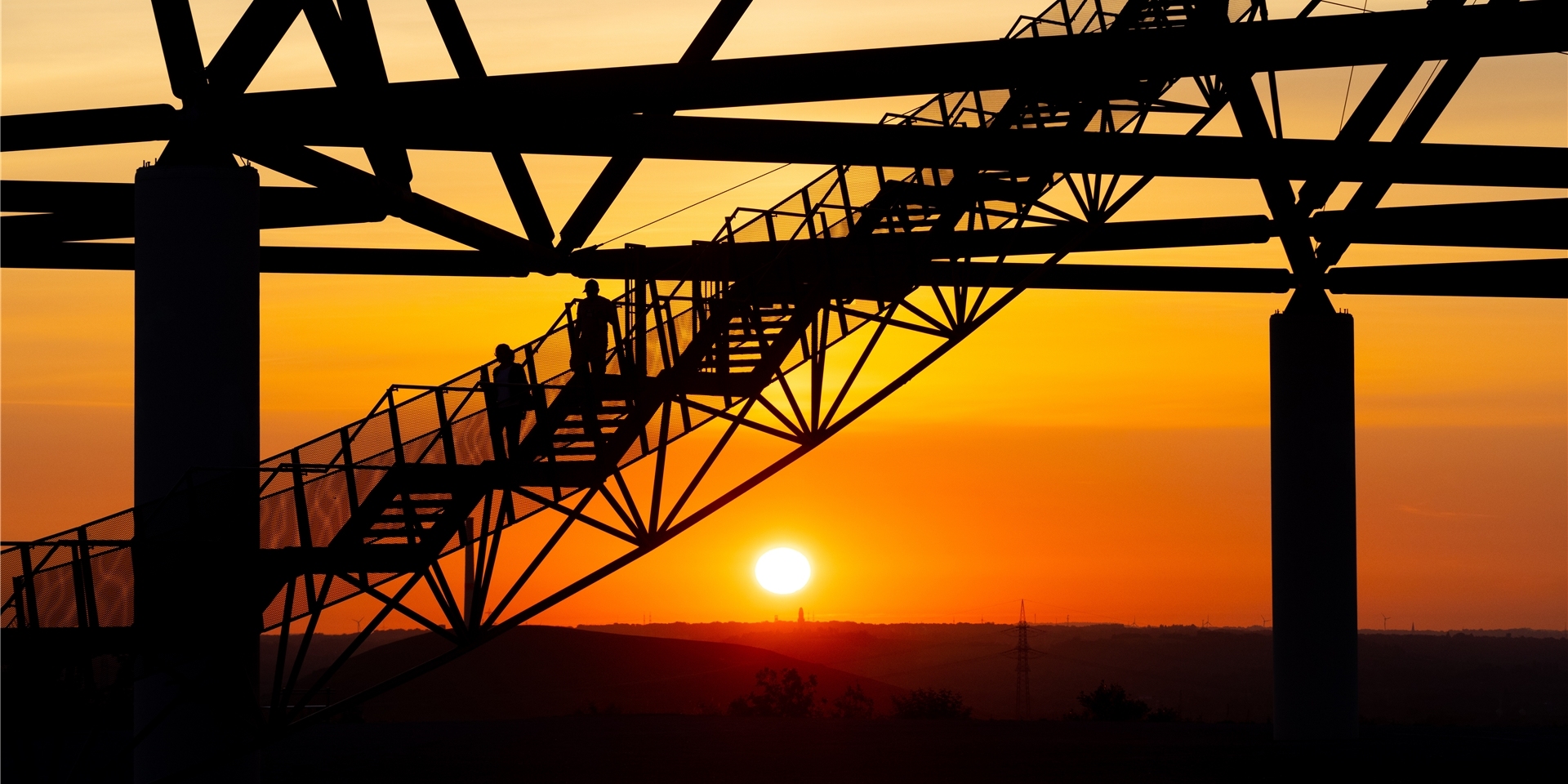 Zwei Menschen laufen bei Sonnenaufgang über eine Treppe des Tetraeders.