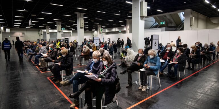 Menschen warten mit Mund-Nasen-Bedeckung in einem Impfzentrum. Die Terminvergabe für die Impfzentren wird in NRW für alle Impfwilligen freigegeben.
