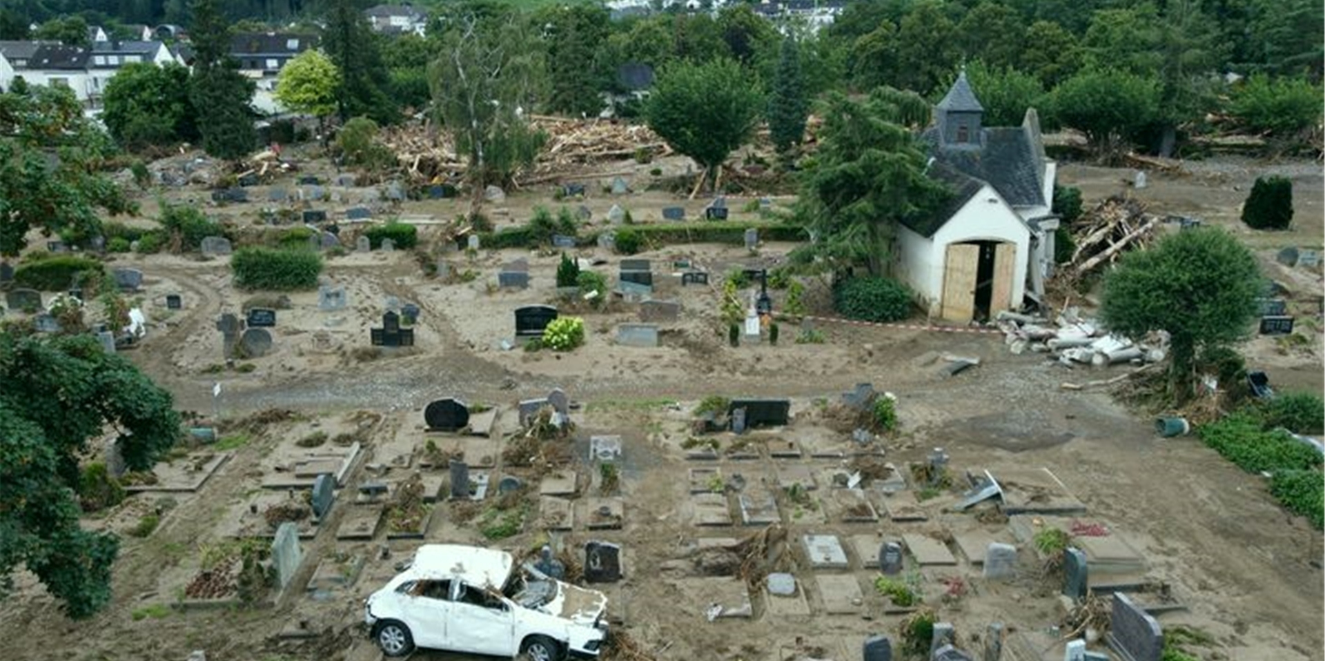 Ein Auto, das im Zuge des Hochwassers auf einen Friedhof geschwemmt wurde, steht nun auf einem verwüsteten Grabfeld. Foto: Thomas Frey/dpa/Archivbild
