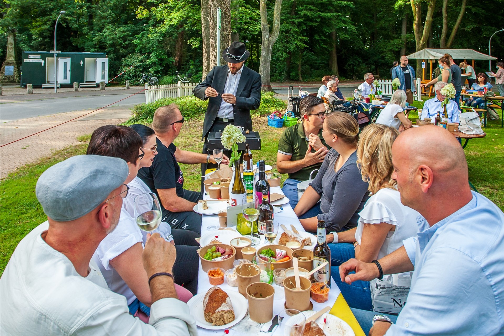 Ein Hütchenspieler steht an einem Tisch, an dem viele Gäste sitzen.