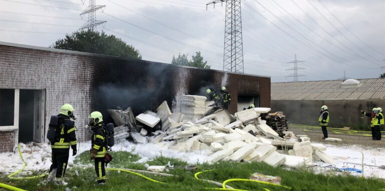 Vor dem Gebäude geraten große Mengen Styroporplatten in Brand. Mit Schaum erstickt die Feuerwehr die Flammen.