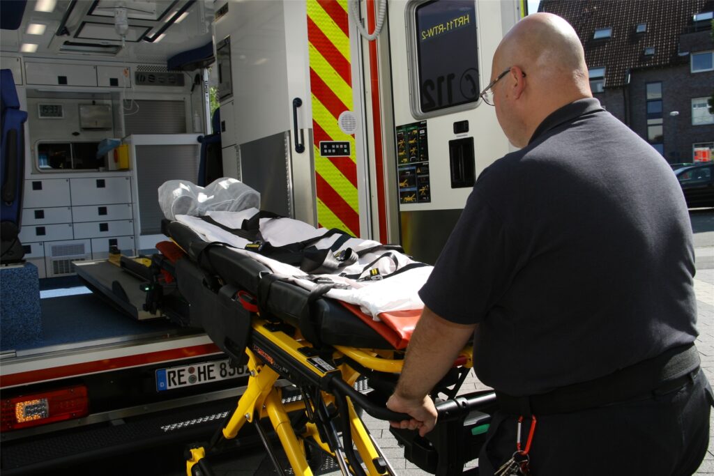 title attribut Die Beine der Trage mit den Rollen fahren sich auf Knopfdruck elektrisch ein und aus. Das rückenschädigende Absenken und Hochheben aus der Hocke und mit Muskelkraft hat ein Ende.