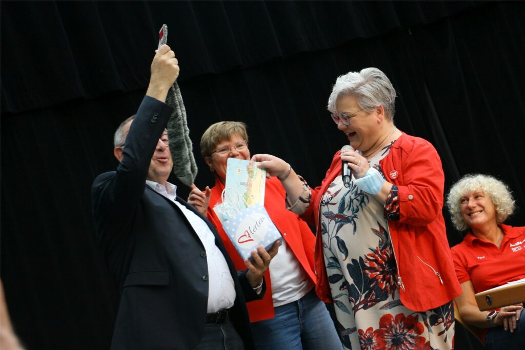 title attribut Die stellvertretende SPD-Vorsitzende Susanne Hardt überreicht Norbert Walter-Borjans eine Geschenktüte, die nicht nur ein Frühstücksbrettchen mit Herten-Motiven enthält, sondern auch graue Socken – in Anspielung auf die Rote-Socken-Kampagne gegen die SPD wegen einer möglichen Koalition mit den Linken. Mit im Bild: die SPD-Vorsitzende Dr. Babette Nieder und Fani Kapetaniou (r.).