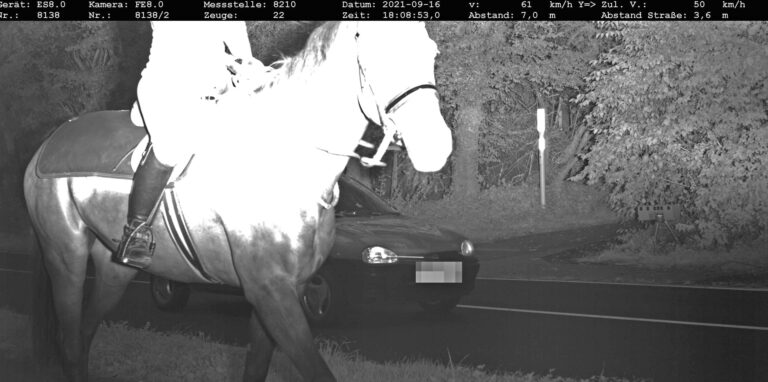 Eine Reiterin wird von einem mobilen Blitzer fotografiert, während im Hintergrund ein Auto mit überhöhter Geschwindigkeit vorbeifährt.