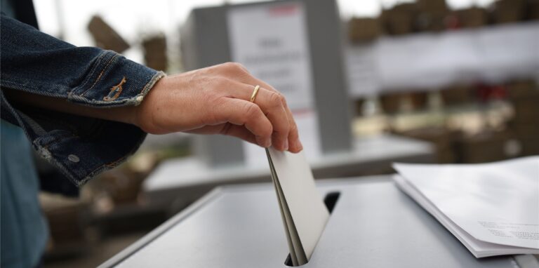 Ein Wahlzettel wird in eine Urne gesteckt.