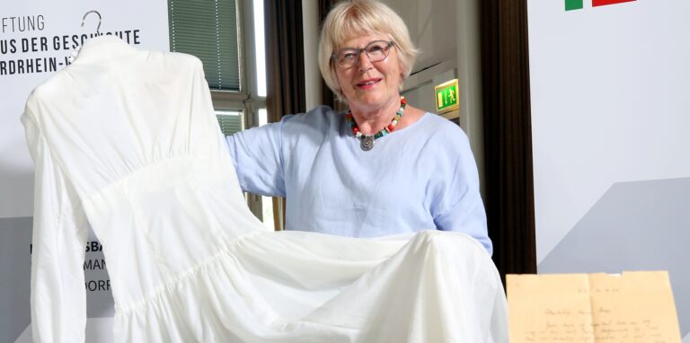 Inge Abresch, Gattin von Sammlungsgründer Werner Abresch, zeigt ein Brautkleid aus Fallschirmseide. Der Bräutigam hatte den Stoff seiner Braut aus Frankreich zur Anfertigung eines Hochzeitskleids schickte. Das Kleid wurde fertig, der Bräutigam aber fiel. Jahre später heiratete die Braut einen anderen Mann – in diesem Kleid. Es ist heute eines der herausragenden Stücke der Sammlung. Auch ein Castrop-Rauxeler Exponat ist dabei.