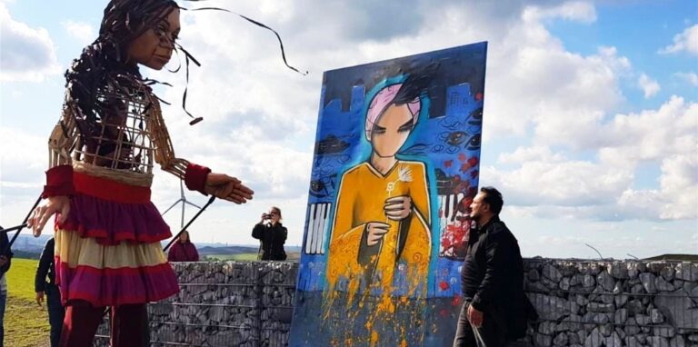 Während der Ruhrfestspiele-Aktion „The Walk“ auf der Halde Hoheward verweilt die Puppe „Amal“ vor dem drei Meter hohen Bild von Künstler Adnan Kassim (r.).