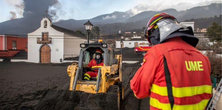 Einsatzkräfte des Militärs entfernen schwarze Asche vom Vulkan, der hinter der kleinen Kirche auf der Kanareninsel La Palma weiter Lava ausstößt.