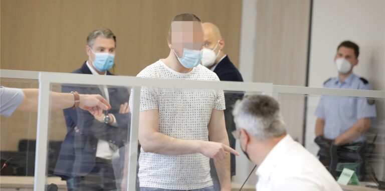 Das Foto zeigt einen der Angeklagten zwischen den Verteidigern.