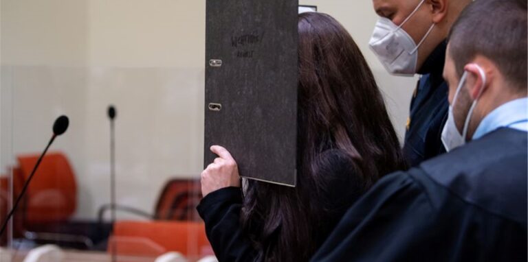 Will nicht gefilmt und fotografiert werden: die Angeklagte Jennifer W. im Gerichtssaal mit einem Ordner vor dem Gesicht.