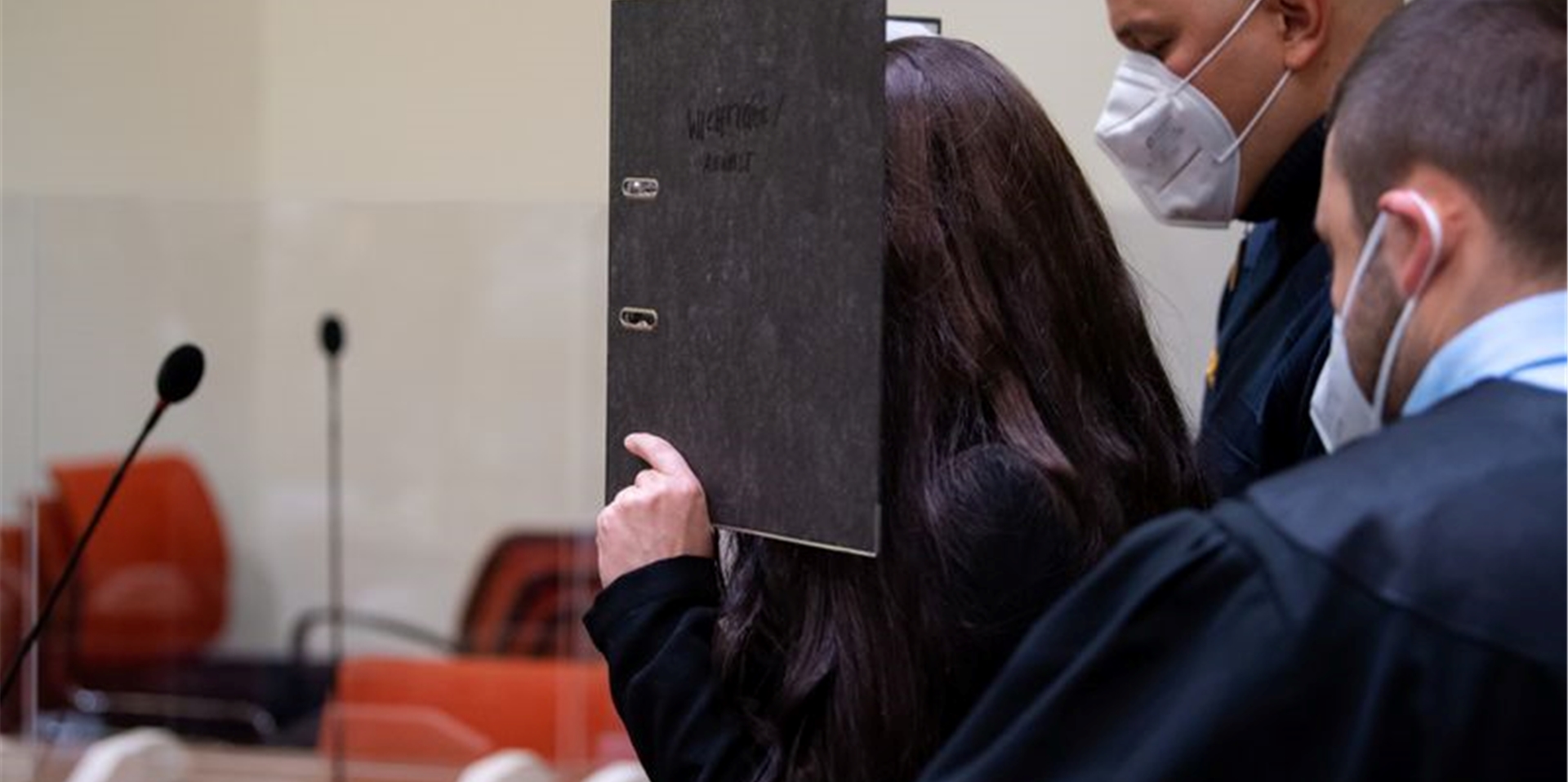 Will nicht gefilmt und fotografiert werden: die Angeklagte Jennifer W. im Gerichtssaal mit einem Ordner vor dem Gesicht.