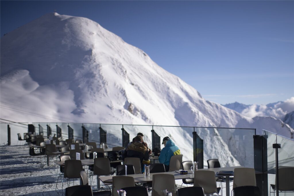 title attribut Gäste sitzen auf der Terrasse eines Bergrestaurants im Skigebiet Silvretta Arena in Samnaun. Das Schweizer Samnaun betreibt mit Ischgl in Tirol (Österreich) ein gemeinsames Skigebiet.