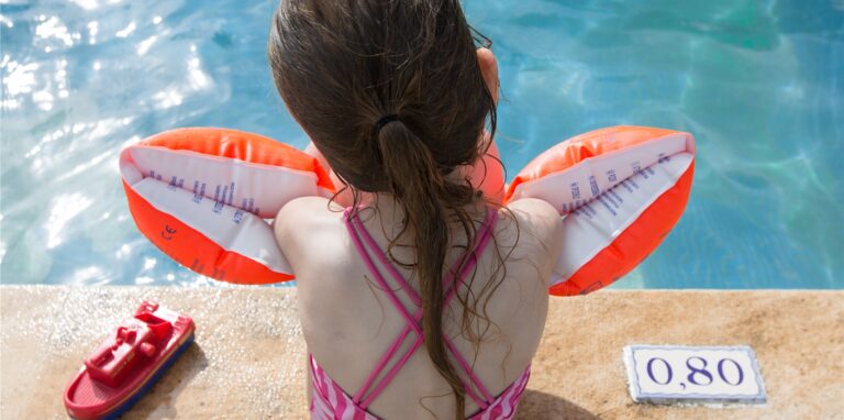 Ein Mädchen mit Schwimmflügeln sitzt an einem Pool