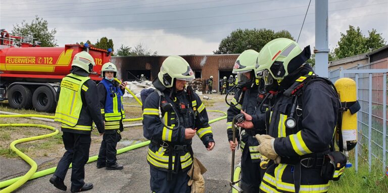Feuerwehrleute stehen vor dem Gebäude, in dem zahlreiche Gasflaschen und Chemikalienkanister lagern, und bereiten sich auf den Einsatz vor.