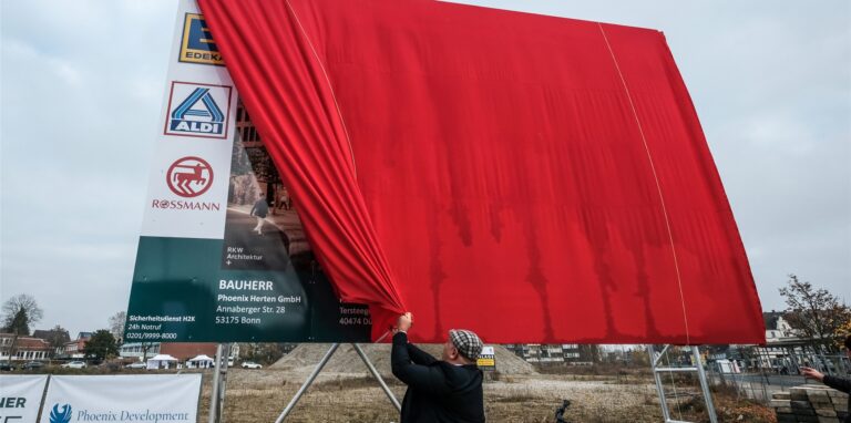 Ein Mitarbeiter enthüllt während des symbolischen ersten Spatenstichs am 24. November das Bauschild für die neuen „Hertener Höfe“ auf der Fläche des früheren Herten-Forums.