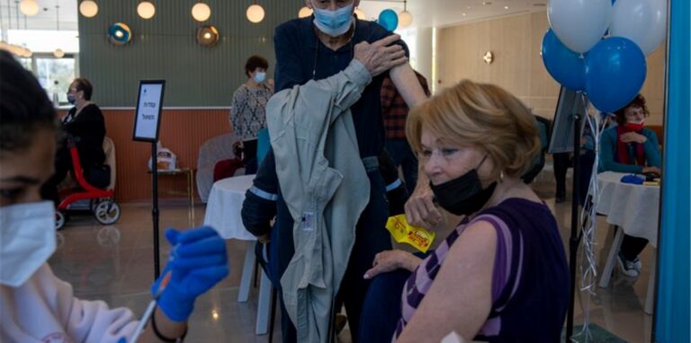 Ein Mann zieht sein Hemd hoch, während seine Frau ihre vierte Dosis des Coronavirus-Impfstoffs in einem privaten Pflegeheim in Petah Tikva erhält.