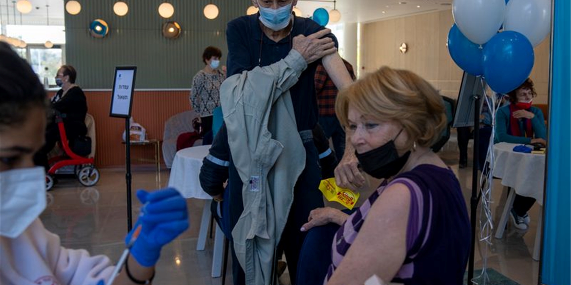 Ein Mann zieht sein Hemd hoch, während seine Frau ihre vierte Dosis des Coronavirus-Impfstoffs in einem privaten Pflegeheim in Petah Tikva erhält.