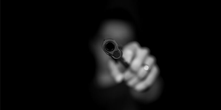 Eine Hand hält die Mündung einer Schusswaffe in Richtung des Betrachters