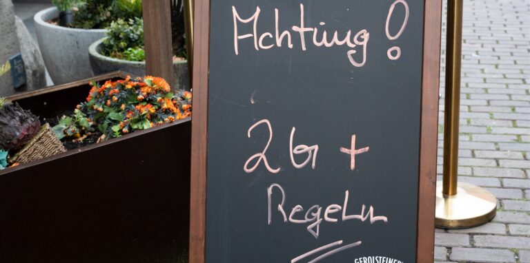 Ein Hinweisschild mit Aufschrift „Achtung! 2G+ Regel“ steht vor einem Restaurant.