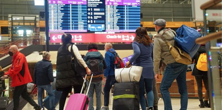 Reisende stehen am Flughafen BER vor einer Info-Tafel.