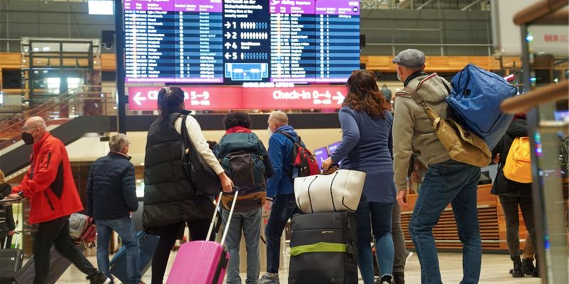Reisende stehen am Flughafen BER vor einer Info-Tafel.