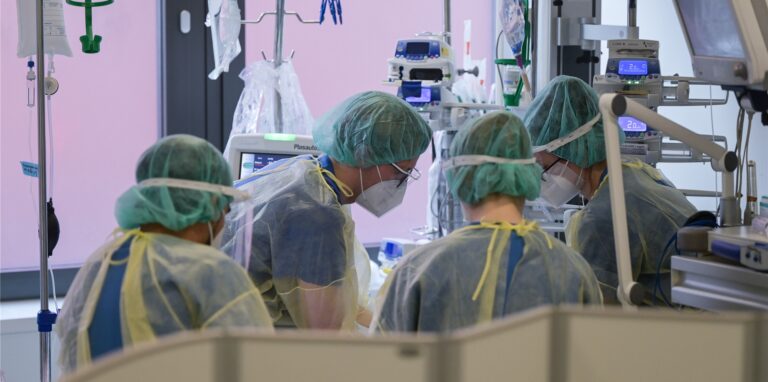 Pfleger und Pflegerinnen sowie eine Ärztin kümmern sich auf der Intensivstation für Corona-Patienten um einen Patienten.