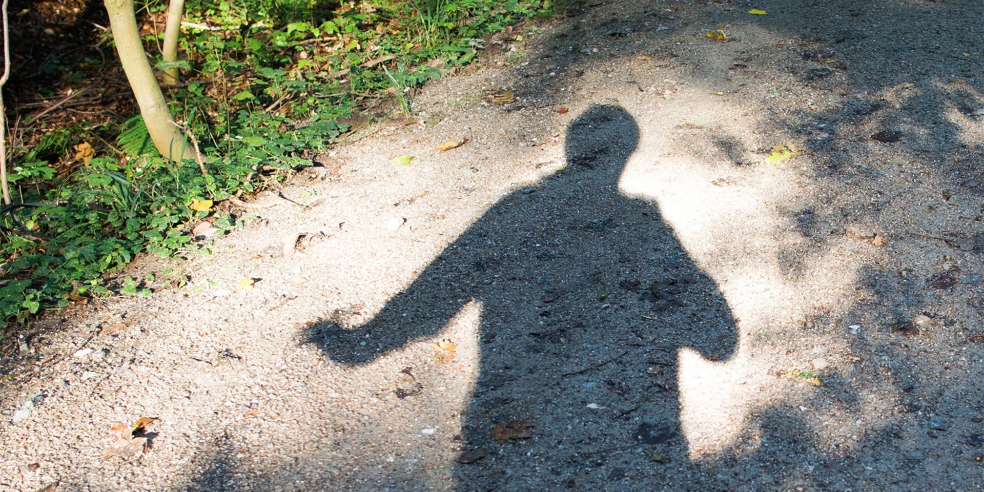 Die Schatten-Silhouette eines Mannes auf einem Spazierweg