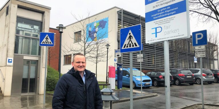 Pflegedirektor Axel Westermann neben einem Schild der Firma Fair Parken, die am Rochus Hospital die Bewirtschaftung des Parkplatzes übernimmt.