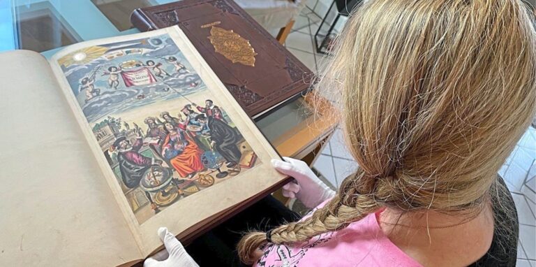 Ute K. präsentiert unserer Redaktion zwei der nachgeahmten historischen Bücher, die ihre Bekannte für viel Geld gekauft hat. Vor ihr aufgeschlagen liegt das Faksimile der „Harmonia Macrocosmica“, daneben der „Atlas Gerardus Mercator“.