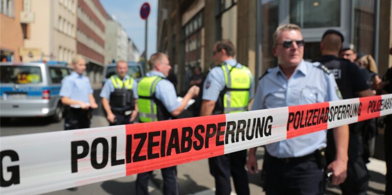 Polizisten stehen vor einem Wohngebäude in der Innenstadt hinter einem Absperrband. (Symbolbild)