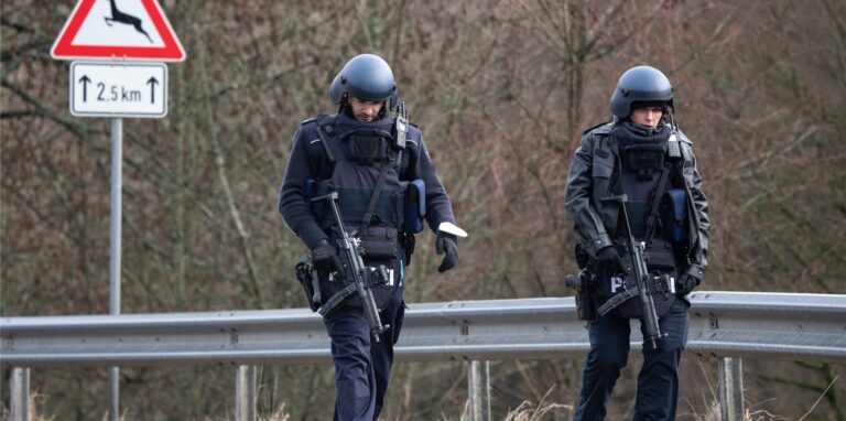 Polizeibeamte gehen an einer Absperrung an der Kreisstraße 22 entlang, rund einen Kilometer von dem Tatort entfernt, an dem zwei Polizeibeamte durch Schüsse getötet wurden. Die tödlichen Schüsse fielen nach Polizeiangaben bei einer routinemäßigen Verkehrskontrolle.