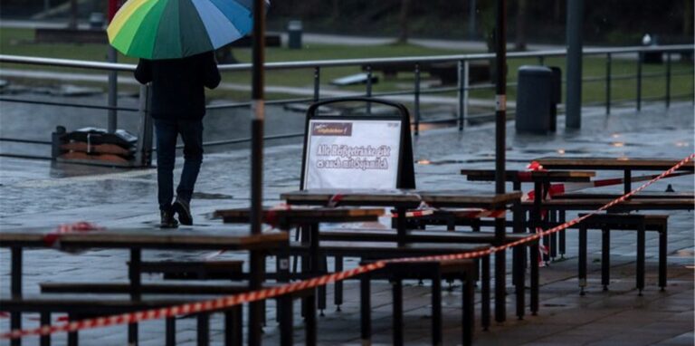 Ein Passant geht unter einem bunten Regenschirm an der Uferprommenade des Phoenix Sees vorbei.
