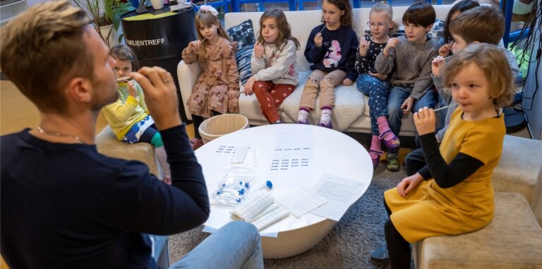 Unter Anleitung eines Kindergärtners machen die Kinder in einer Kindertagesstätte eine Corona-Pooltestung (Lollitest).