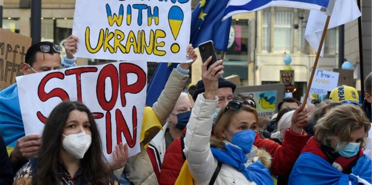 Demonstranten halten Schilder mit der Aufschrift „#Stand with Ukraine“.