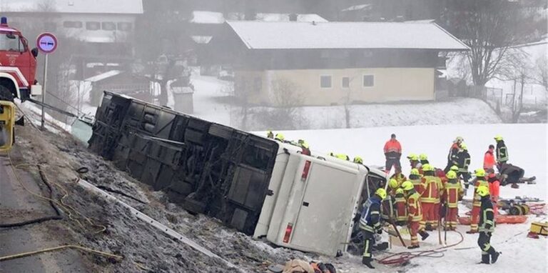Einsatzkräfte der Feuerwehr stehen neben einem umgekippten Reisebus am Straßenrand.