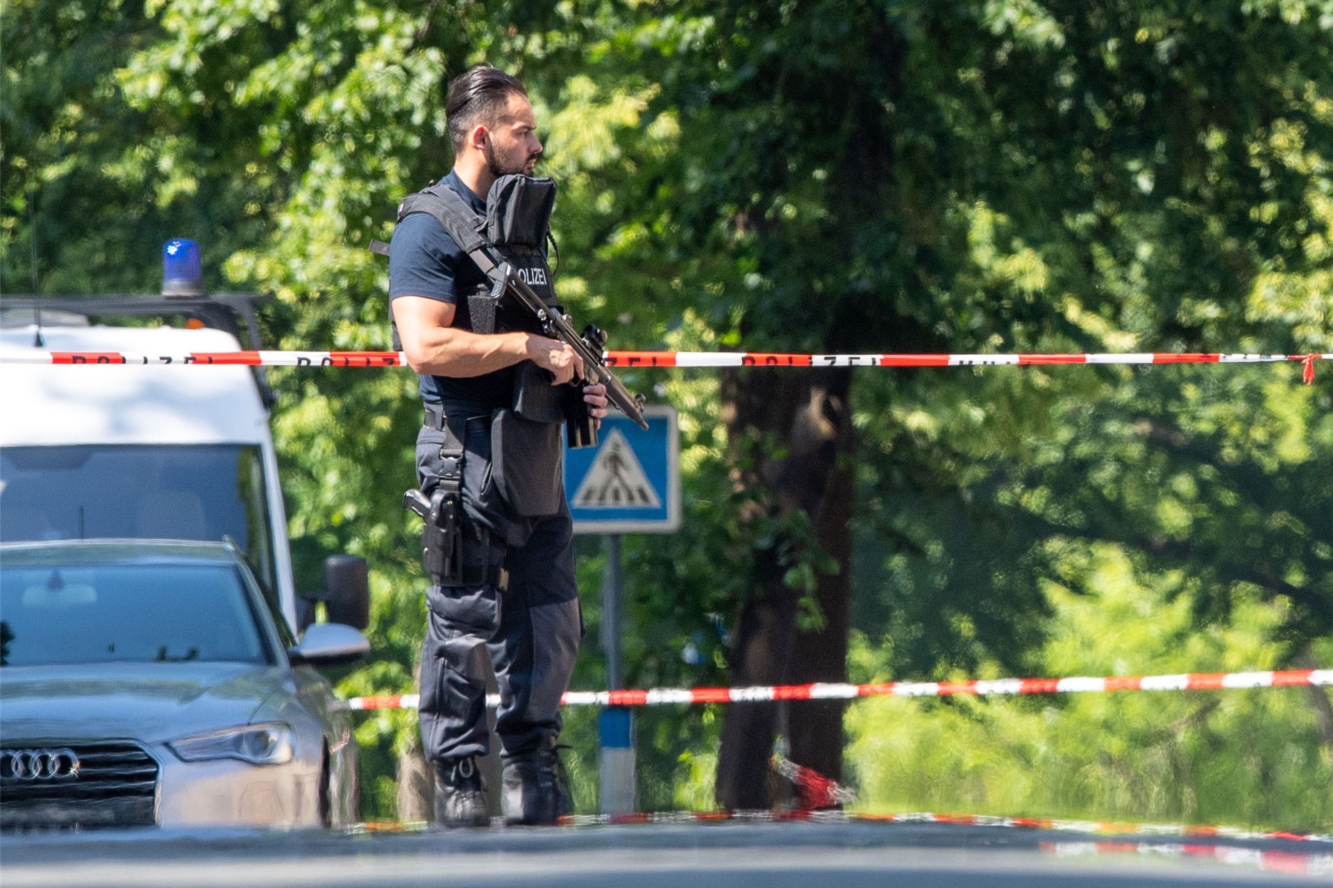 Ein Polizist mit Schutzweste und Gewehr steht an einer Absperrung in Espelkamp. In Espelkamp sind nach Angaben der Bielefelder Polizei zwei Menschen erschossen worden.
