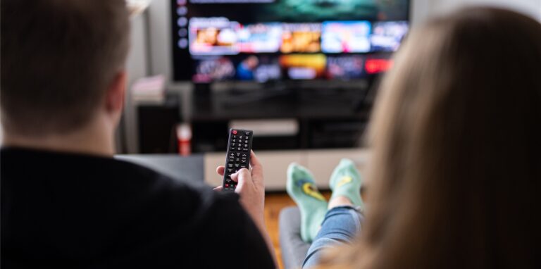 Ein Paar sitzt vor dem Fernseher und guckt Netflix, der Mann hält die Fernbedienung. (Symbolbild)