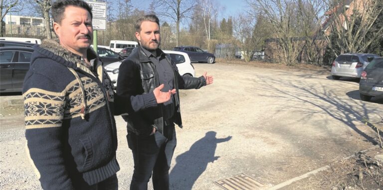 Sergej Tarde (links) und sein Sohn Dennis stehen auf dem Lehrerparkplatz an der Gartenstraße und deuten auf die Fläche, die laut erster Planung für die neue Flüchtlingsunterkunft angedacht war. Direkt dahinter steht ihr Eigenheim.