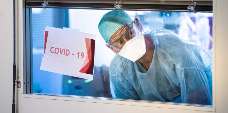 Ein Krankenhaus-Mitarbeiter schaut neben einem Schild mit der Aufschrift „Covid-19“ aus dem Fenster einer Intensivstation. Im Kreis Recklinghausen werden dort wieder deutlich mehr Menschen behandelt, als noch vor einer Woche.