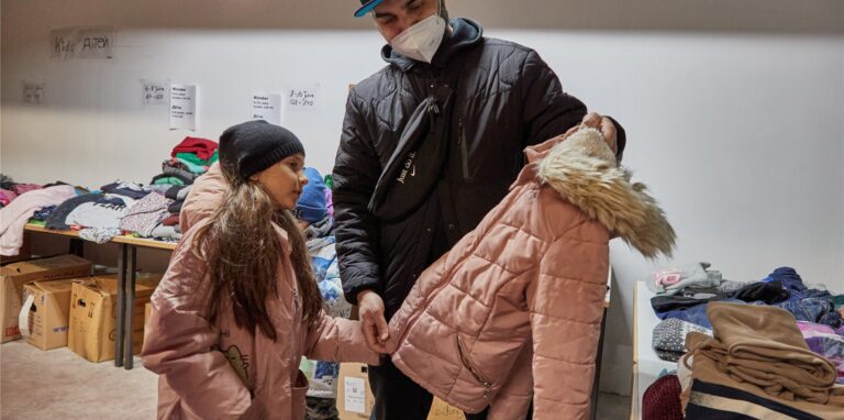 Der ukrainische Flüchtling Mohamed Jazara steht mit seiner Tochter Jasmina in der Kleiderkammer in Rissen und betrachtet einen Mantel.