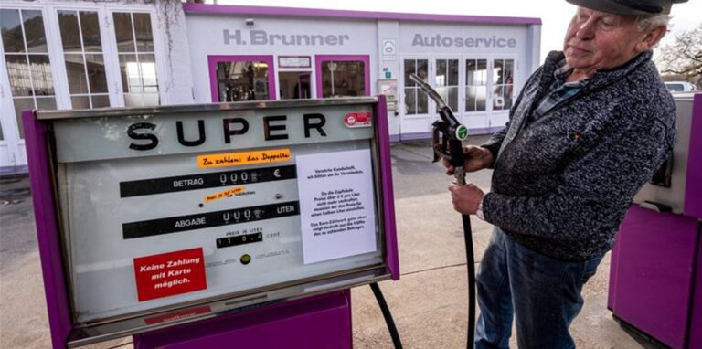 Hans Brunner steht an einer Zapfsäule seiner Tankstelle. Die Tankstelle zeigt Benzin- und Dieselpreise halbliterweise an.