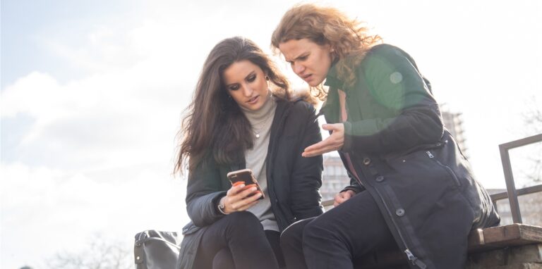 Zwei Frauen schauen auf ihr Handy (Symbolbild). Aus einem Video, das aktuell kursiert, geht hervor, dass eine Gruppe einen Jugendlichen im Bereich Euskirchen zu Tode prügelt. Eine Frau sagt auf russischer Sprache, dass sie von dem Vorfall gehört habe. Die Polizei warnt vor dem Video.