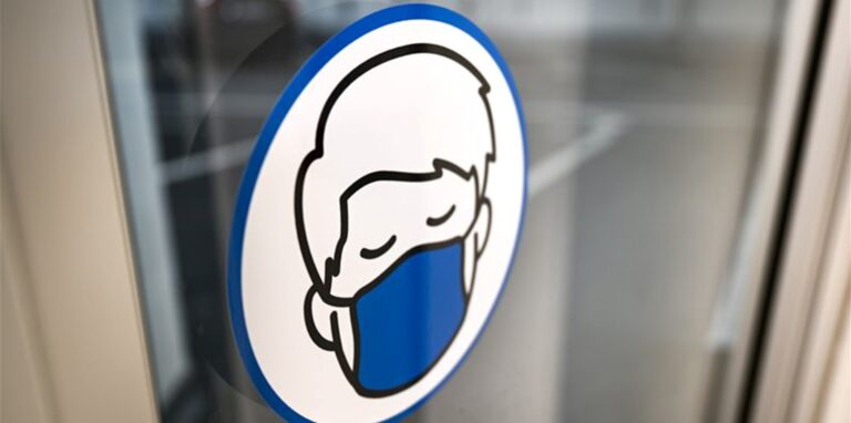 Ein Aufkleber an einer Glastür weist auf das Tragen einer Maske hin.