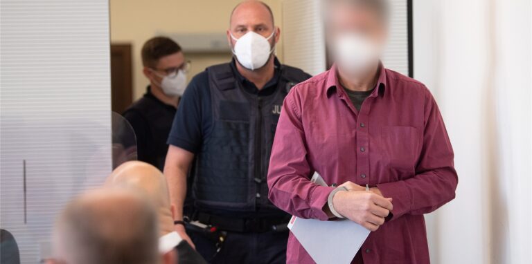 Der Angeklagte (r) wird in Handschellen in den Gerichtssaal gebracht. Der Mann hat die Tat gestanden, im vergangenen Jahr in Bad Kreuznach einen Mitarbeiter einer Tankstelle erschossen zu haben, nachdem dieser ihn auf die coronabedingte Maskenpflicht hingewiesen hatte.